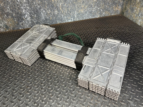 Folded Quickstep 10-foot tactical assault ladders placed side by side on a textured metal floor. Each ladder features closely packed rungs made from silver-colored metal, bound together by black and green straps, highlighting their compact and portable design ideal for emergency or military use.