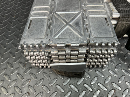 Extreme close-up of the hinge and joint area of a Quickstep 10-foot tactical assault emergency ladder. The image highlights the intricate assembly of metallic rungs and locking mechanisms on the ladder's folded section, set against a textured diamond-patterned metal surface.