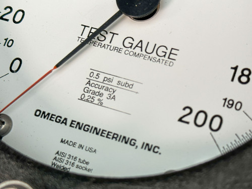 This close-up image shows the lower portion of an Omega pressure gauge with detailed text. The gauge, labeled "TEST GAUGE - TEMPERATURE COMPENSATED," indicates specifications including "0.5 psi subt" and "Accuracy Grade 3A 0.25%." The face of the gauge also displays "OMEGA ENGINEERING, INC." and "MADE IN USA." The gauge has a range of 0-200 PSI and is part of the 4.5" Type T model, PGT-45L-200.