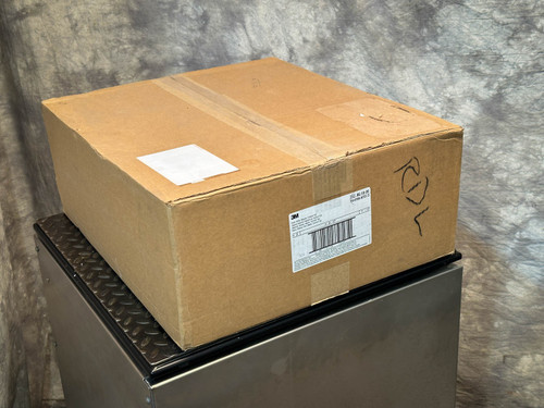 A sealed cardboard box labeled with shipping and product information, resting on a metal surface. PAPR Hood BE-10-20 available from Obtainium Science & Industry Surplus.