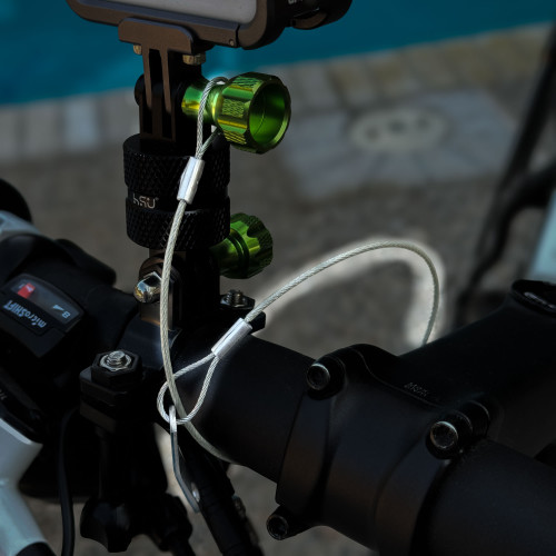 Close-up view of a GoPro Mount action camera's securing mechanism on a bicycle handlebar, featuring green adjustment knobs and a safety tether. The background includes a swimming pool. GoPro Mount action camera safety tether from Obtainium Science and Surplus.