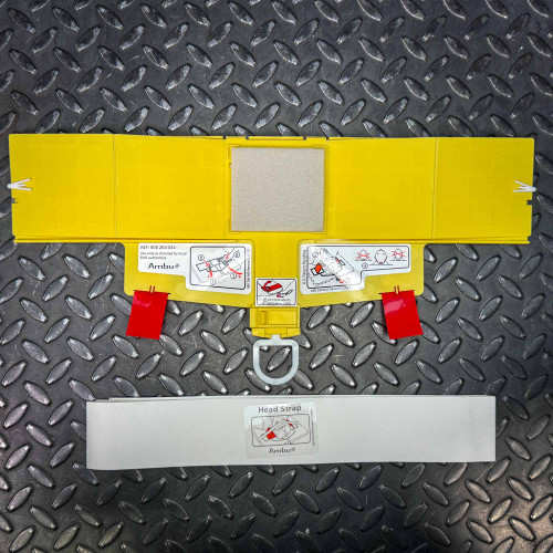 The image shows a yellow Ambu Head Wedge cervical immobilization device laid out flat on a textured metal surface. The device includes several panels with diagrams demonstrating how to use it, such as applying head straps and positioning the head correctly. The diagrams are clearly labeled, making them easy to understand.