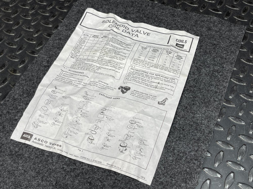 An instruction sheet related to the ASCO Replacement Coil 222345-009-D, laid out flat on a textured surface with metal flooring visible underneath.