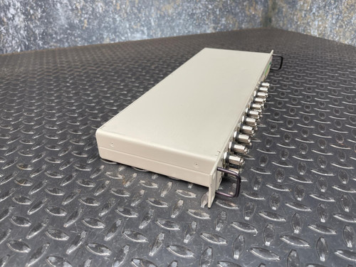 A side view of the National Instruments BNC-2090 terminal block, showing its plain white surface and row of BNC connectors on a textured metal surface. This BNC Terminal Block is available from Obtainium Science & Industry Surplus.