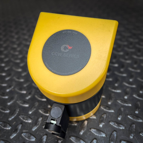 Top view of the yellow housing of the Crowd Control Warehouse Magnetic Retractable Belt Barrier from Obtainium Science and Surplus, featuring a round branding emblem with a circular design on a dark background.