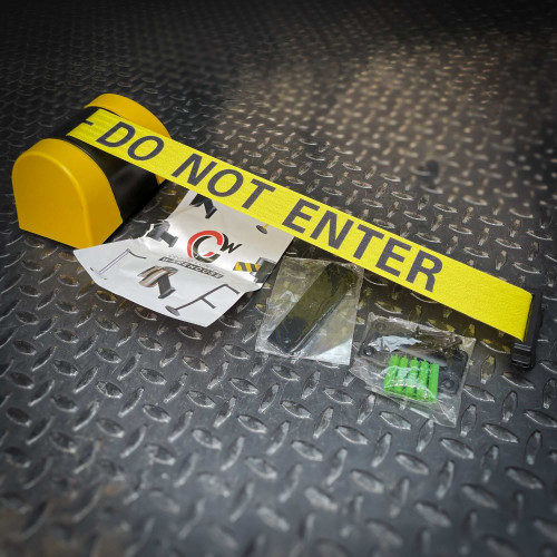 A Crowd Control Warehouse Magnetic Retractable Belt Barrier from Obtainium Science and Surplus, displayed on a textured metal surface with packaging accessories including screws and wall mounts.