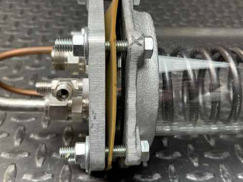 Detailed side view of the custom-made vacuum/pressure chamber’s end, highlighting the layered gaskets, bolts, and connectors of the Obtainium Science and Surplus model. The coiled heat-exchange tubing is visible within the transparent chamber.