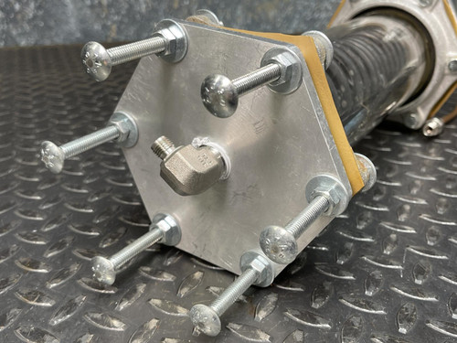 Close-up of one end of the Obtainium Science and Surplus custom vacuum/pressure chamber, showing the metal end plate, long bolts, and a central connector for pressure or vacuum adjustments.