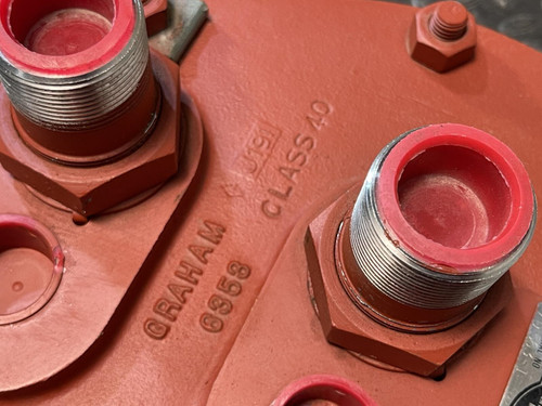 Close-up view of the red end plate on the Graham heat exchanger from Obtainium Science and Surplus, highlighting engraved markings such as “Graham” and “Class 20” near the two main threaded ports with red protective caps.