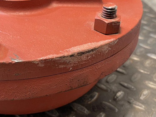 Detailed view of the outer edge of the Graham heat exchanger from Obtainium Science and Surplus, showing wear and minor scratches on the red painted surface, with a bolt visible on the top edge of the component.