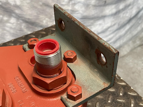 Close-up of the Graham heat exchanger's bracket from Obtainium Science and Surplus, focusing on one of the main ports with red protective cap and surrounding bolts, along with the mounting bracket on the metal base.