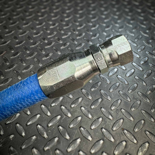 A close-up of the JIC hydraulic fitting on the opposite end of a blue Aeroquip FC300 hose from Obtainium Science and Surplus, showing the outer surface of the fitting against a textured metal background.