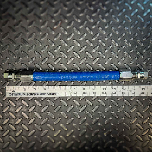 A blue Aeroquip FC300 hose with JIC hydraulic fittings from Obtainium Science and Surplus, positioned alongside a ruler on a textured metal surface to show the hose's length.