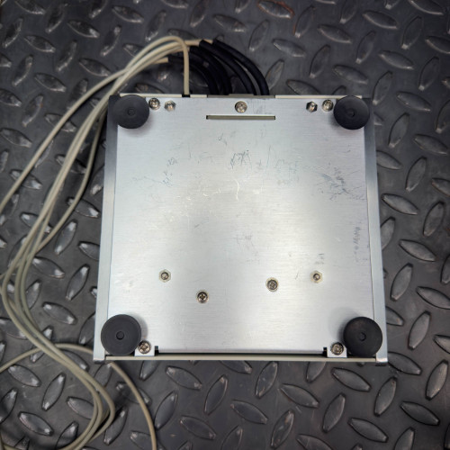 Bottom view of the Hewlett Packard 16021A Test Fixture showing the underside with rubber feet and some cables.