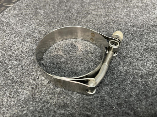 A close-up of a single Clampco 2.5" stainless T-bolt clamp lying flat on a gray textured surface. The clamp's sturdy metal band and the T-bolt mechanism are visible, showing its industrial-grade design from Obtainium Science and Surplus.