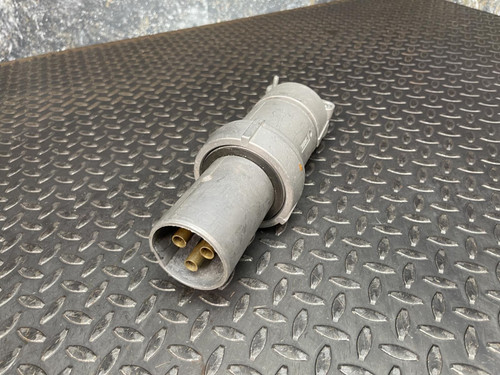 Angled view of an Appleton 100A plug from Obtainium Science and Surplus, highlighting the open end with brass connector pins inside a cylindrical metal casing, placed on a metal surface.