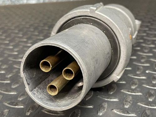 Close-up of an Appleton 100A plug from Obtainium Science and Surplus showing three brass connector pins inside a cylindrical metal casing, placed on a metal surface.