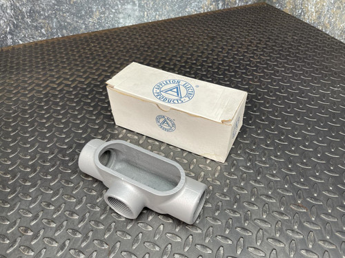 T conduit body from Obtainium Science and Surplus placed next to its original packaging box on a metal surface.