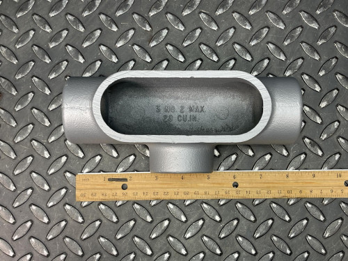 T conduit body from Obtainium Science and Surplus on a metal surface with a ruler placed next to it for scale.