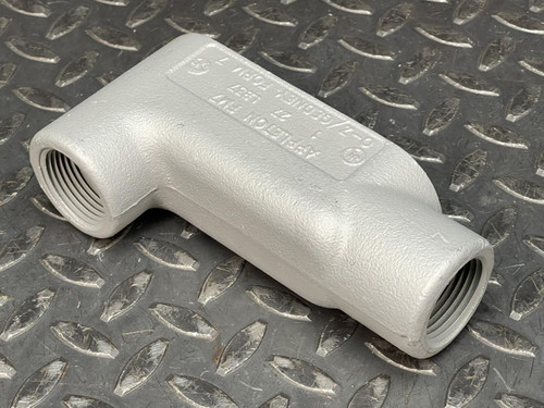 Angled side view of a 1" Appleton LB Conduit Body from Obtainium Science and Surplus on a diamond plate surface, showing the threaded openings.
