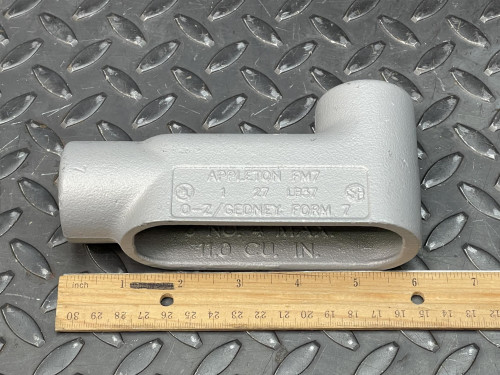 Side view of a 1" Appleton LB Conduit Body from Obtainium Science and Surplus on a diamond plate surface, with a wooden ruler placed next to it for scale.