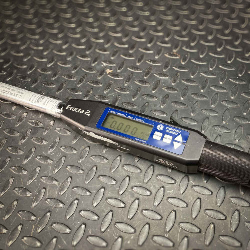 Close-up view of the Sturtevant Richmont Exacta 2 digital torque wrench on a textured metal surface. The display shows "0.000" and is surrounded by various control buttons for setting and storing torque measurements, emphasizing precision and digital control.