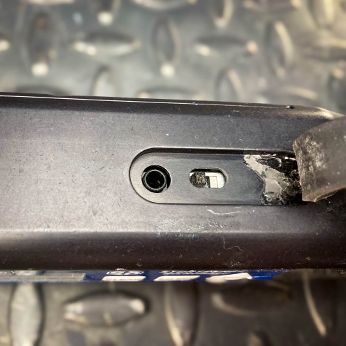 Close-up view of a port on the Sturtevant Richmont Exacta 2 digital torque wrench. The image shows a small circular port and a sliding switch, highlighting the tool's connectivity and adjustment features. The tool is placed on a textured metal surface, available from Obtainium Science & Industry Surplus.