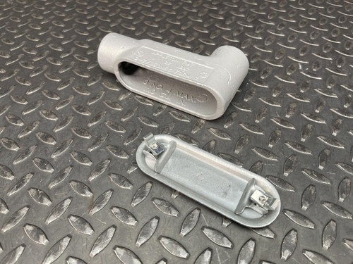 A 1" Appleton LB37 Conduit Body from Obtainium Science and Surplus shown on a diamond plate surface, alongside its detachable cover with two screws.