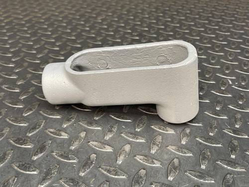 Side view of a 1" Appleton LB37 Conduit Body from Obtainium Science and Surplus on a diamond plate surface, showing its oval shape and open cavity.