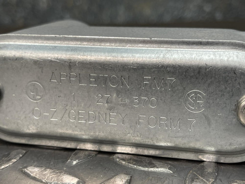 Another view of the 1" Appleton LB37 Conduit Body from Obtainium Science and Surplus with the cover attached, placed on a diamond plate surface.