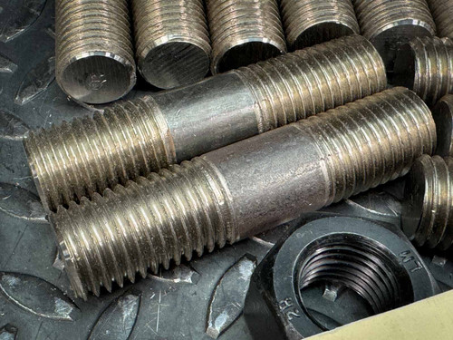 Close-up image of two B7 stud bolts, showing detailed threading and a hex nut in the background. These bolts are part of a 12-pack, each measuring 4.5 inches by 1 inch with 8 UNC threading. Available from Obtainium Science & Industry Surplus.