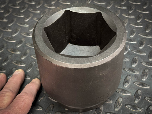 A close-up of a large, hexagonal metal socket with a hand for scale, lying on a textured metal surface. This item is available from Obtainium Science & Industry Surplus.