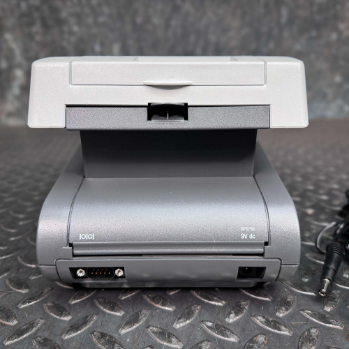 The image presents the back view of the Siemens CLINITEK Status+ Analyzer, highlighting its connectivity and power ports. The analyzer features a standard power port labeled "9V dc" and various interface ports that could be used for data transmission or connecting to other devices. The design emphasizes practicality and ease of integration into a clinical laboratory setting, with a sturdy base and minimalistic rear panel. This setup ensures that the device can easily be set up and connected within a variety of medical environments.
