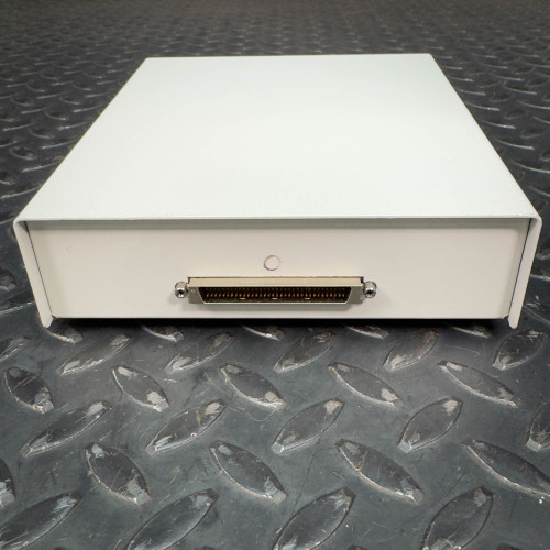The image depicts the back side of a National Instruments SCB-68 terminal block connector. The white rectangular device is shown on a textured metal surface, featuring a single connector port centrally located on the back panel. The design is minimalist, with no additional visible markings or labels from this angle.
