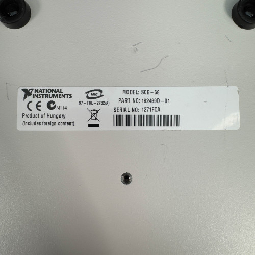 The image shows a close-up of a label on the bottom of a National Instruments SCB-68 terminal block connector. The label contains various details including the National Instruments logo, the model number "SCB-68," the part number "182849B-01," the serial number "127170A," and a note that the product is made in Hungary. There are also CE and recycling symbols visible on the label.