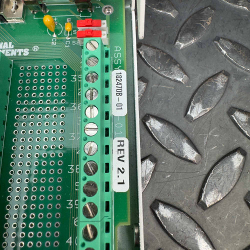 Close-up of the green circuit board inside the National Instruments SCB-68 I/O terminal block connector, showing the assembly number 182470B-01 and revision number REV 2.1, placed on a black textured metal surface. The device is available from Obtainium Science & Industry Surplus.