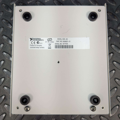 Bottom view of the National Instruments SCB-68 I/O terminal block connector, showing product information including model SCB-68, part number 182469D-01, and serial number 1271FCA, placed on a black textured metal surface. This terminal block connector is available from Obtainium Science & Industry Surplus.