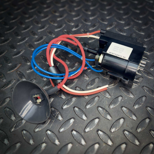 A vintage CRT monitor flyback transformer from Obtainium Science & Industry Surplus, showing a black component with attached red and blue wires on a textured metal surface.