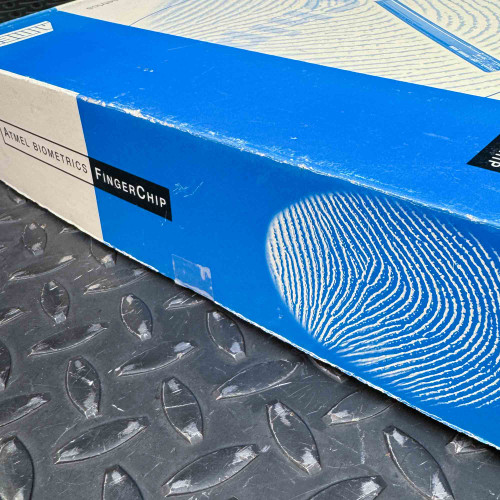 Side view of the ATMEL Biometric FingerChip development board kit box from the Obtainium Science Surplus Store, showing the blue and white design with a fingerprint graphic.