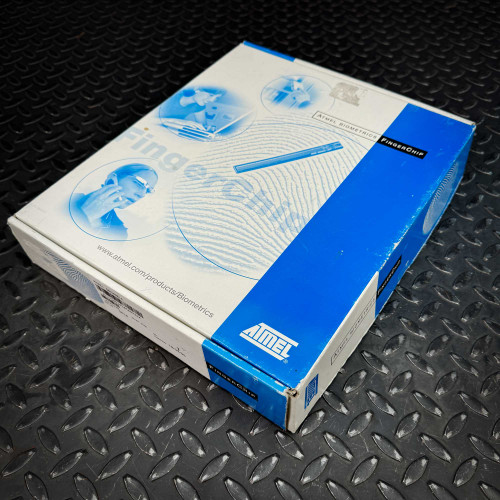 Full view of the ATMEL Biometric FingerChip development board kit from the Obtainium Science Surplus Store, displaying the box with various blue-toned images and product information.