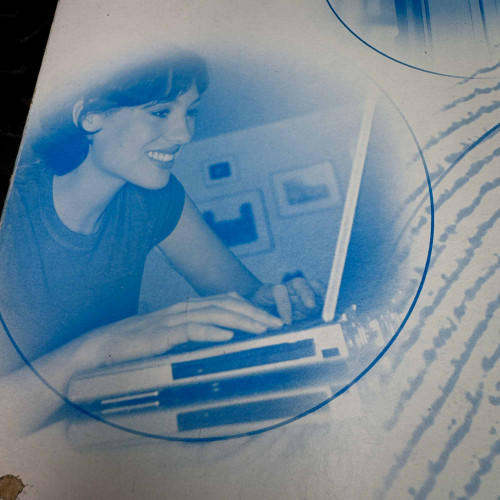 Blue-toned image of a woman using a laptop, featured on the packaging of the ATMEL Biometric FingerChip development board kit from the Obtainium Science Surplus Store.
