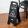 Black Rubbermaid Executive 2-Sided Multi-Lingual Caution Sign Situated by a Table