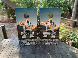"Custom mountain-themed cornhole boards featuring a rustic wood and stone design with a scenic mountain backdrop, bold monogram initial, and personalized last name. Perfect for outdoor enthusiasts, cabin retreats, and rustic weddings "Custom mountain-themed cornhole boards featuring a rustic wood and stone design with a scenic mountain backdrop, bold monogram initial, and personalized last name. Perfect for outdoor enthusiasts, cabin retreats, and rustic weddings