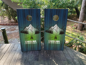 Custom mountain-themed cornhole boards featuring a blue and green gradient wood background, a scenic mountain illustration, and personalized campground name. Perfect for camping enthusiasts, outdoor retreats, and nature lovers Custom mountain-themed cornhole boards featuring a blue and green gradient wood background, a scenic mountain illustration, and personalized campground name. Perfect for camping enthusiasts, outdoor retreats, and nature lovers