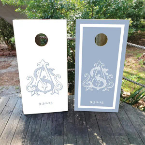 These cornhole boards feature a refined and elegant design. One board is white with a light blue monogram in the center, while the other is light blue with a white border and matching monogram. Perfect for a wedding or special occasion.