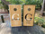 Two personalized cornhole board wraps featuring a sleek woodgrain background, large initial 'G' with elegant script names 'Mercedes' and 'Austin,' and additional text reading 'Gratz est. 2023,' bordered with contrasting white and black frames, with white scoring holes near the top."