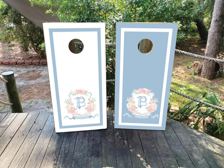 Elegant monogram wedding cornhole board wraps in dusty blue and white, featuring a refined crest design with initials “A & B,” family name “The Devines,” and wedding date “10.17.2025.” These sophisticated vinyl wraps include a laurel wreath motif and classic border detailing—perfect for timeless, romantic wedding décor.