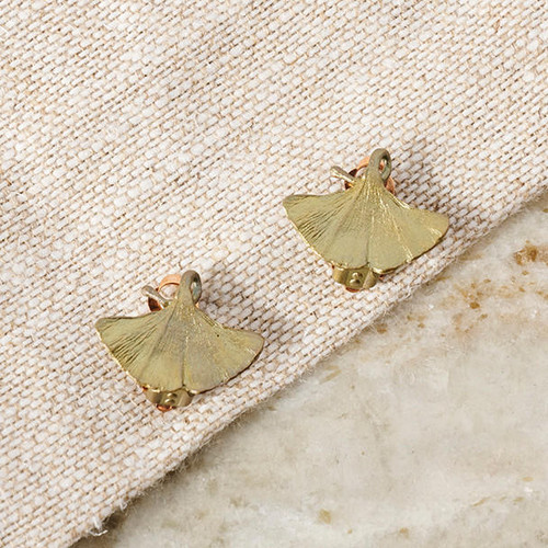 Front view of a pair of bronze gingko leaf-shaped clip-on earrings laid on linen fabric.
