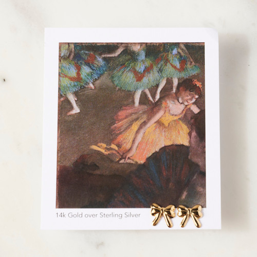 Card with white border printed with Degas image with 2 small gold bow shaped earrings pinned to lower right corner of card