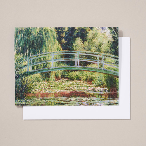 A notecard featuring an impressionist painting of a footbridge over a pond with waterlilies with trees in the background is shown on top of a white envelope.
